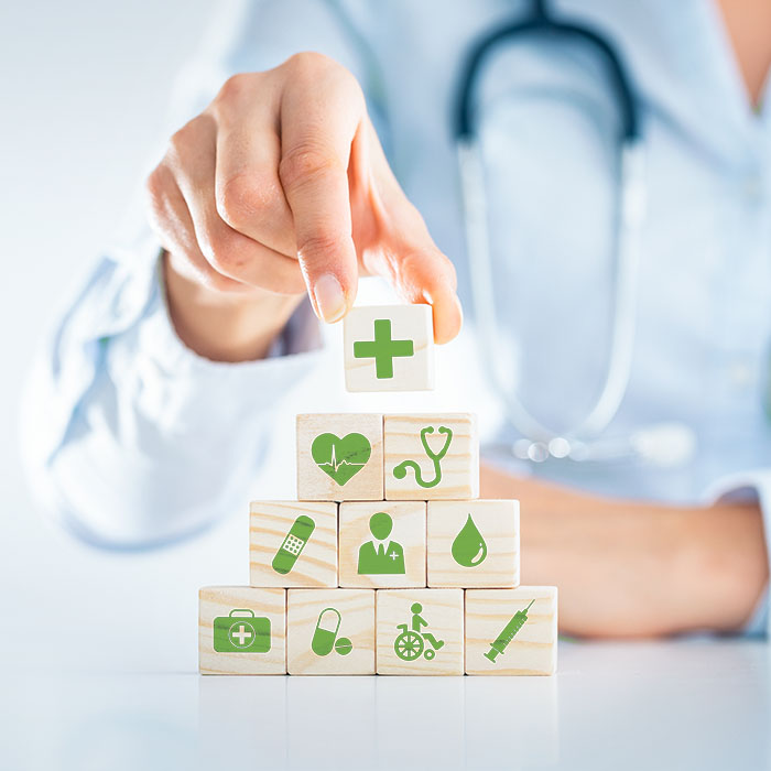 Ärztin baut mit Holzklötzchen eine kleine Pyramide auf ihrem Tisch. Auf der Pyramide sind grüne Symbole abgebildet, die die Gesundheitsleistungen widerspiegeln.
