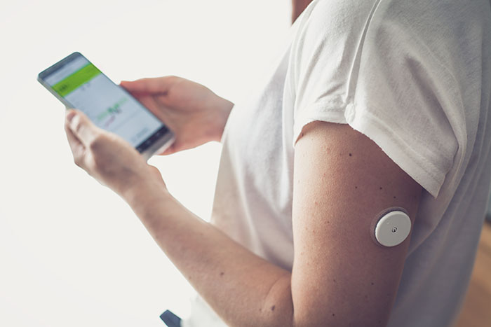 Frau untersucht ihren Blutzuckerwert anhand einer Mobiltetefon-App und einem Patch auf dem Arm.